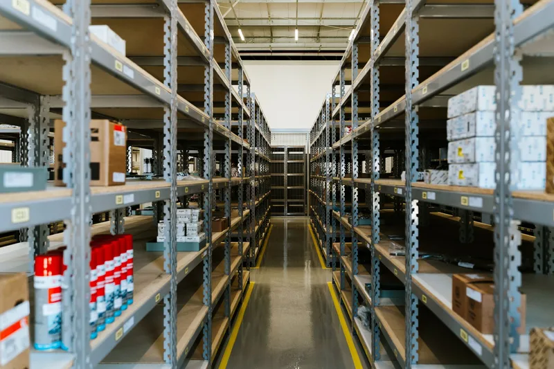 Aisle of metal shelving stocked with boxes and supplies in a small warehouse