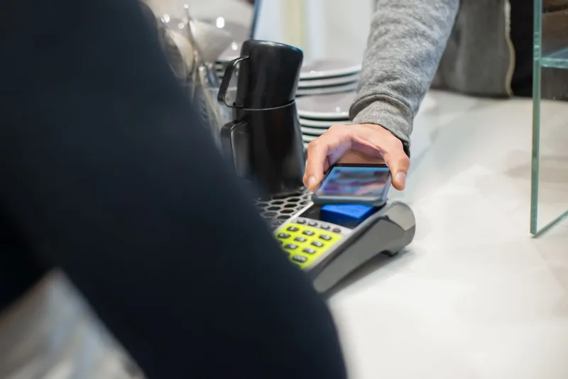A customer makes a contactless payment using a smartphone at a café